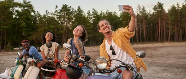 Jóvenes felices, motociclistas sonriendo mientras se toman una selfie juntos, sentados en scooters fuera de la ciudad — Foto de Stock