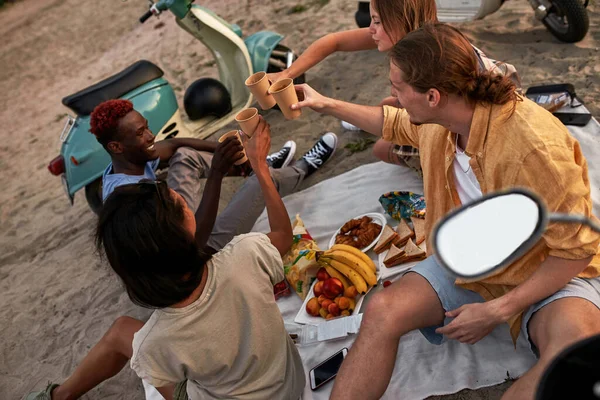 Grupo de jóvenes disfrutando de un picnic en la playa. Amigos teniendo fiesta de verano al atardecer — Foto de Stock
