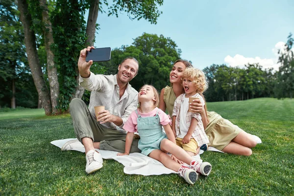 快乐的家庭在户外度过时光，一起拍照时使用智能手机，夏天在大自然中野餐 — 图库照片