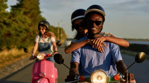 Alegre casal jovem diverso montando uma scooter e se divertindo ao pôr do sol — Fotografia de Stock