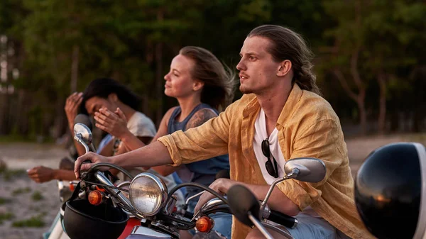 Caucasian young guy, motorcycle rider looking away, spending time together with his friends outside the city