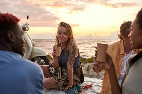 Attraktiv ung kvinna njuter av picknick på stranden. Olika vänner som har sommarfest vid solnedgången — Stockfoto