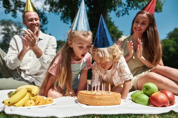 Joyeux famille portant des chapeaux de fête, profiter de célébrer l'anniversaire des enfants dans le parc un jour d'été. Enfants soufflant des bougies sur un gâteau — Photo