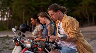 Odaklanmış genç bir adam, akıllı telefon kullanan motosiklet sürücüsü şehir dışında arkadaşlarıyla vakit geçirirken, scooter 'da oturuyor.