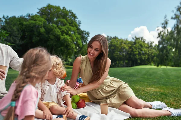 Hermosa mamá relajándose junto con la familia al aire libre, teniendo picnic en la naturaleza en un día de verano —  Fotos de Stock