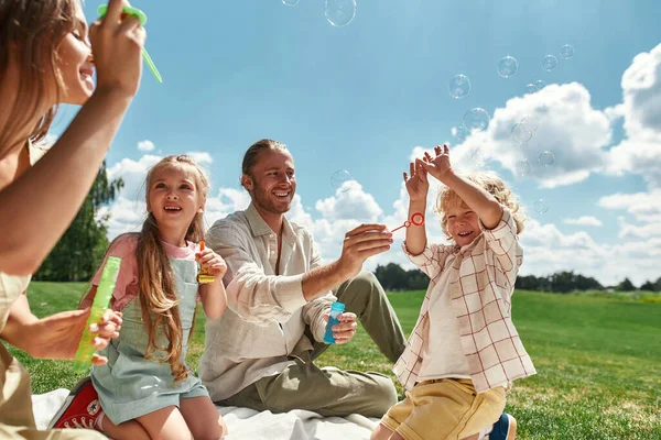 两个孩子一边和父母在一起一边玩乐，一家人夏天在大自然中野餐 — 图库照片