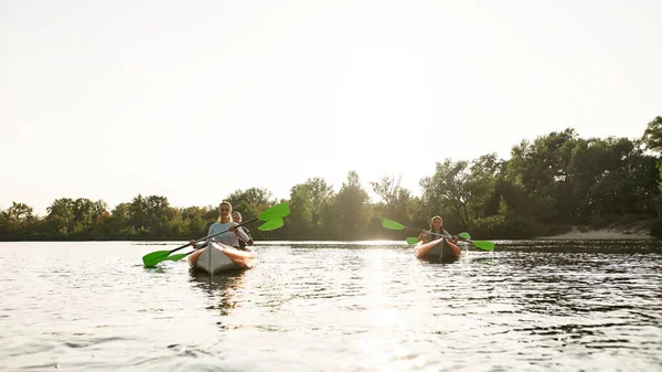 Hevesli gençler bir nehirde kürek çekiyorlar, hafta sonlarını dışarıda geçiriyorlar.
