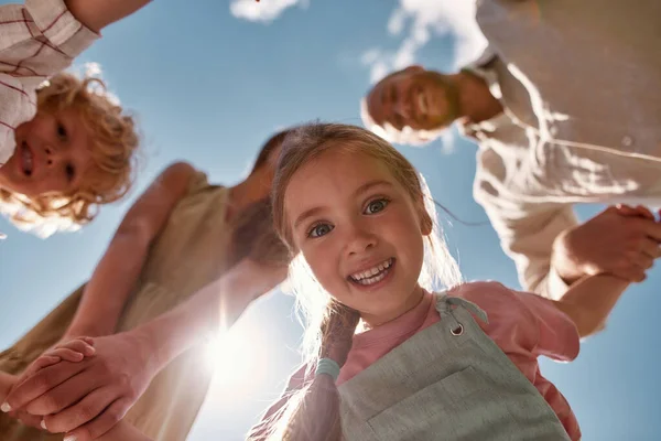 Retrato de la adorable niña sosteniendo a los padres y las manos del hermano mientras mira hacia abajo a la cámara con el cielo azul arriba —  Fotos de Stock
