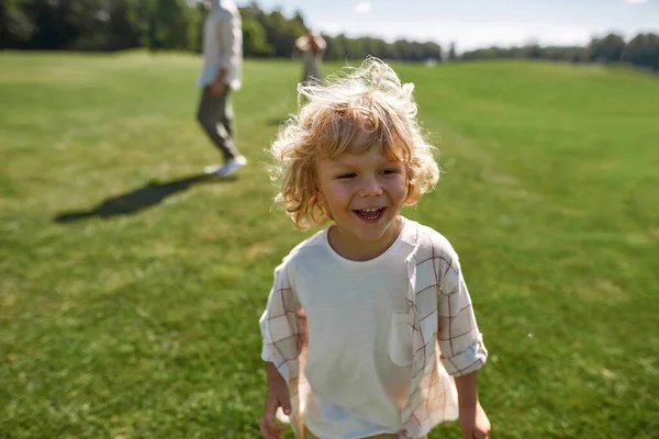Портрет чарівного маленького хлопчика, який посміхається, граючи разом з батьками в зеленому парку в літній день — стокове фото