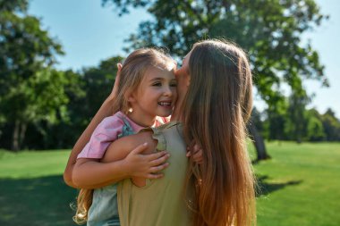 Sevgi dolu anne, küçük tatlı kızına sarılıyor, onu kucaklıyor ve yaz parkında dinleniyor.