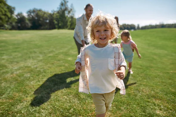 Vreugdevol jongetje glimlachend terwijl hij op een zomerdag vangbal speelt met zijn ouders en zus in het groene park. Gelukkig gezin genieten van vrijetijdsbesteding — Stockfoto