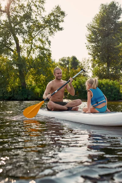 Padre insegna a suo figlio, figlia minore sup surf su un fiume immerso nella splendida natura in una giornata estiva — Foto Stock