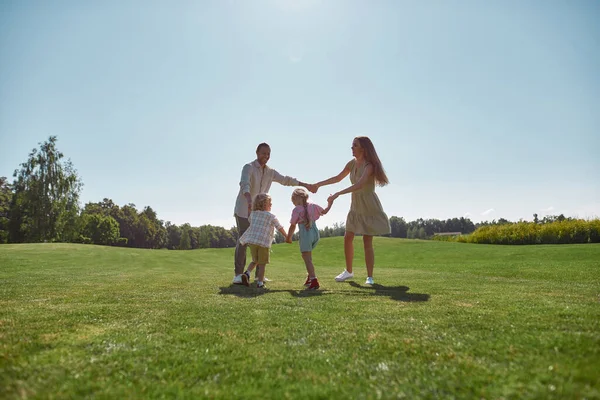 Padres activos pasando tiempo juntos con dos niños pequeños, niño y niña en el parque verde en un día de verano. Familia feliz disfrutando de la actividad de ocio — Foto de Stock