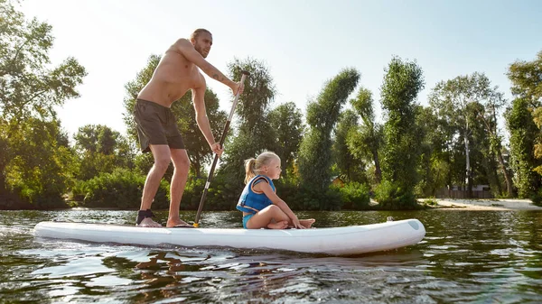 Vader samen met zijn dochtertje ontspannen, sup surfen op een rivier midden in de prachtige natuur op een zomerse dag — Stockfoto