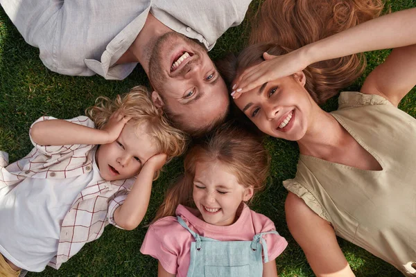 Vista superior de la familia feliz con lindos niños pequeños relajándose, tumbado sobre hierba verde en el parque de verano —  Fotos de Stock