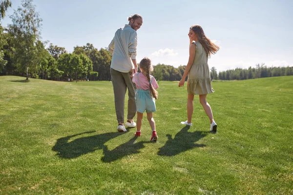 활동적 인 어린 소녀는 부모님 과 함께 즐거운 시간을 보내며, 여름날푸른 공원에서 부모님을 잡습니다 — 스톡 사진