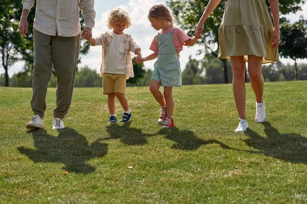 어린 부모와 두 어린 아이가 손을 잡고 녹색의 여름 공원 밖에서 함께 걸어 나오는 총에 맞은 사진 — 스톡 사진