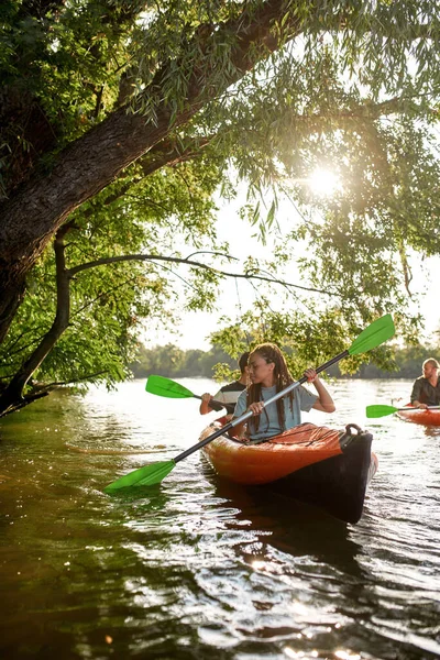 Abenteuerlustige Freunde paddeln im Frühling oder Sommer gemeinsam auf dem Fluss, umgeben von Bäumen — Stockfoto