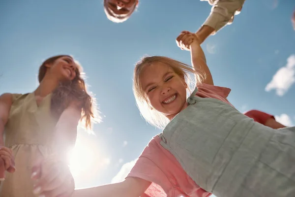 Porträtt av lycklig liten barn flicka tittar ner och ler mot kameran medan hon håller sina föräldrar händer — Stockfoto