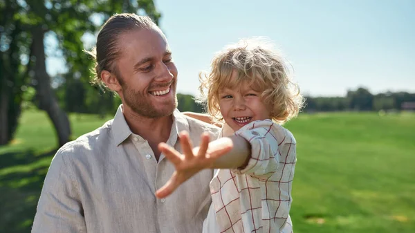 Mutlu genç baba, bir yaz günü parkta oynarken gülümsüyor ve oğlunu kucağına alıyor. — Stok fotoğraf