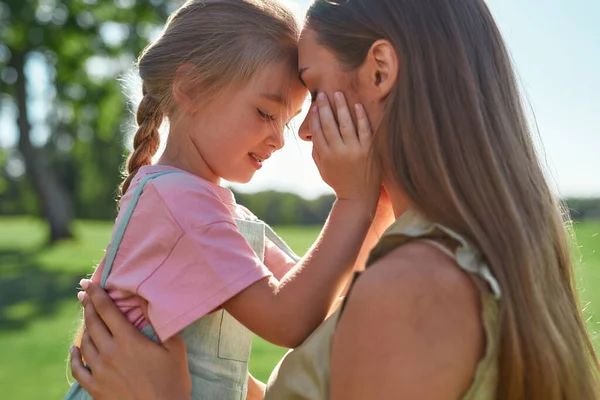 Närbild porträtt av kärleksfull ung mor hålla hennes söta lilla dotter samtidigt tillbringa tid tillsammans i sommarparken — Stockfoto