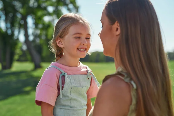 Закрыть портрет милой маленькой дочки, улыбающейся, проводя время вместе с заботливой мамой в летнем парке — стоковое фото