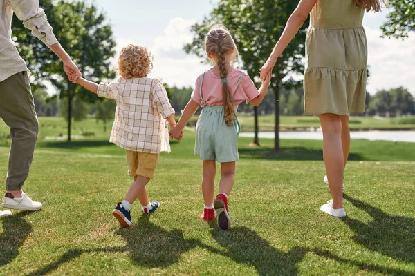 Καλλιεργημένη φωτογραφία μιας χαρούμενης νεαρής οικογένειας να κρατιέται χέρι-χέρι, περπατώντας μαζί έξω στο πράσινο καλοκαιρινό πάρκο — Φωτογραφία Αρχείου