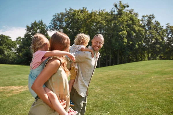 Niños pequeños, niños y niñas disfrutando de un paseo en la espalda de sus padres. Familia caminando en el verde parque de verano — Foto de Stock