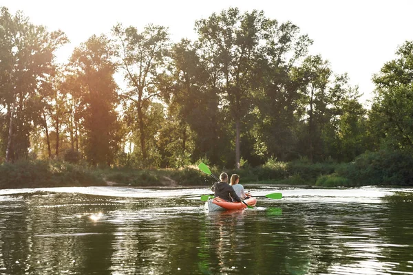 Genç çift, huzurlu yaz doğasıyla çevrili bir gölde birlikte kayıkla geziyor.
