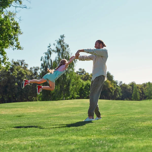 Plan complet de jeune père et fille s'amusant ensemble, tenant la main et filant sur le champ d'herbe dans le parc d'été — Photo