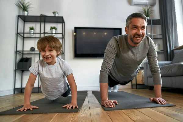 Lachende actieve vader en zoon trainen samen thuis — Stockfoto