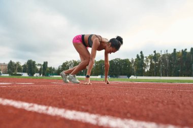 Stadyumdaki atletizm sahasında başlayan profesyonel bayan koşucunun yan görüntüsü