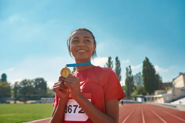 Glada unga kvinnliga idrottare ler bort och håller sin guldmedalj när de står på banan — Stockfoto