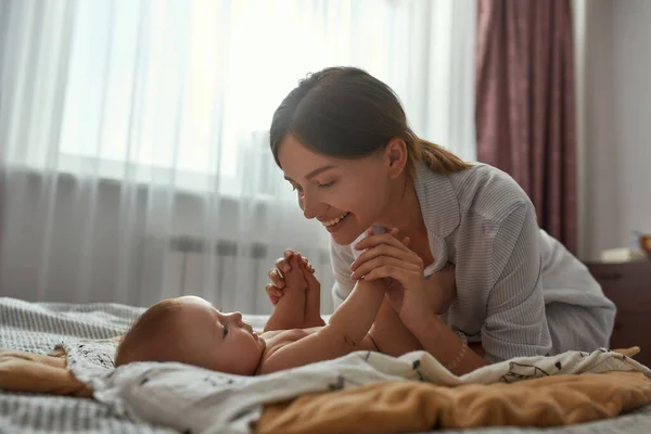 Charming mother happily smiling, looking at baby — Stock Photo, Image