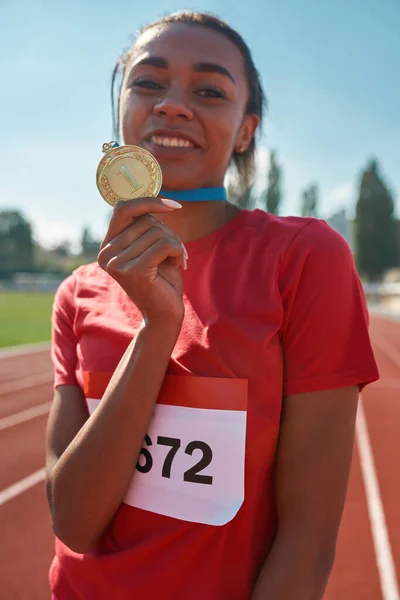 Porträtt av tävlingsinriktad ung kvinnlig idrottsman ler mot kameran och visar sin guldmedalj när hon står på tävlingsbanan — Stockfoto