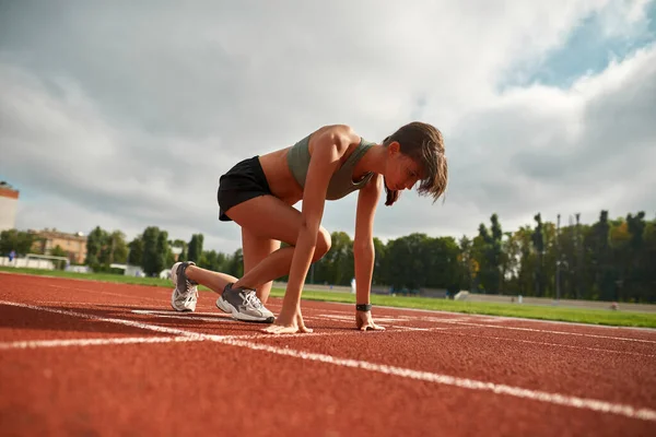 Koncentrerad ung kvinnlig idrottsman redo att starta loppet på stadion på dagtid — Stockfoto