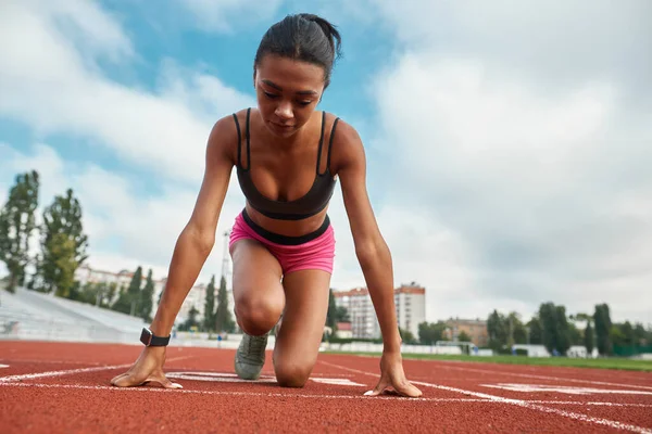 Vista de ángulo bajo de corredor joven profesional en ropa deportiva listo para correr en el campo de atletismo en el estadio — Foto de Stock