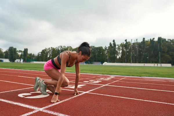 Corredor joven profesional en ropa deportiva preparándose para comenzar a correr en el campo de atletismo en el estadio — Foto de Stock