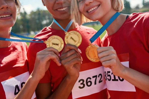 Närbild skott av unga kvinnliga idrottare ler, håller och visar sina guldmedaljer, står tillsammans på banan — Stockfoto