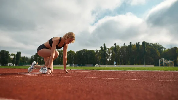 Motiverad ung idrottskvinna redo att starta loppet på stadion på dagtid — Stockfoto