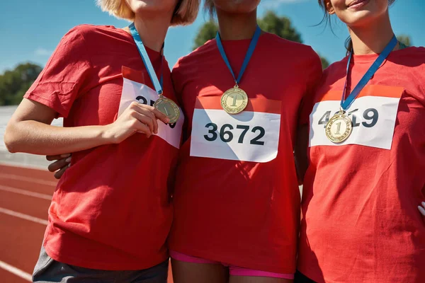 Beskärda skott av unga kvinnliga idrottare bär guldmedaljer, står tillsammans på banan — Stockfoto