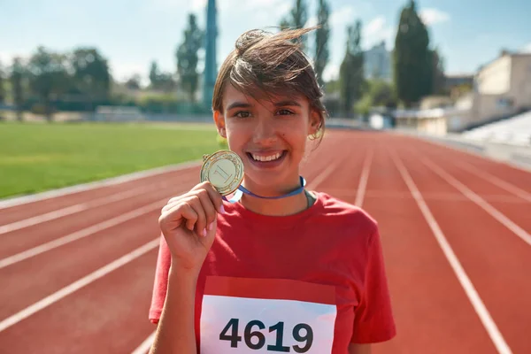 Retrato de uma jovem corredora feliz sorrindo para a câmera e mostrando sua medalha de ouro enquanto estava na pista de corrida — Fotografia de Stock