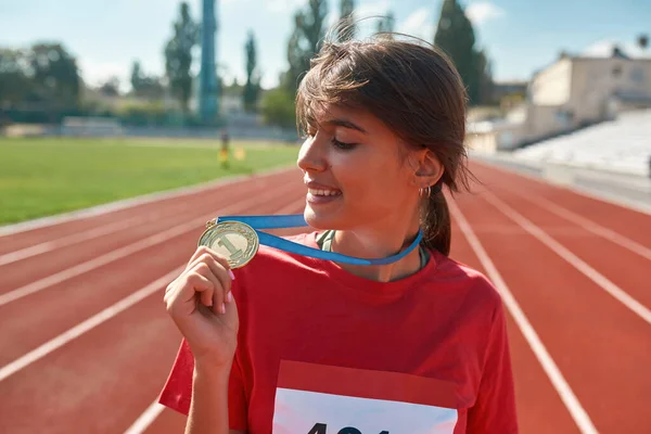 Härlig ung idrottskvinna ler och visar sin guldmedalj när hon står på arenan — Stockfoto