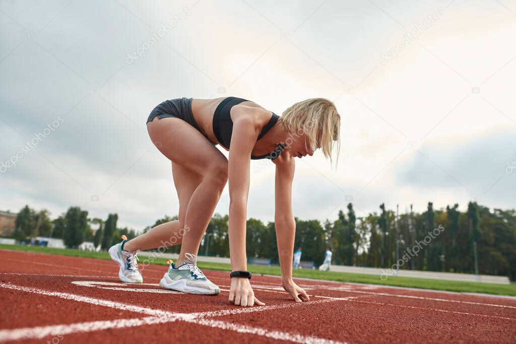 Side view of professional young sportswoman ready to start running on track field at stadium