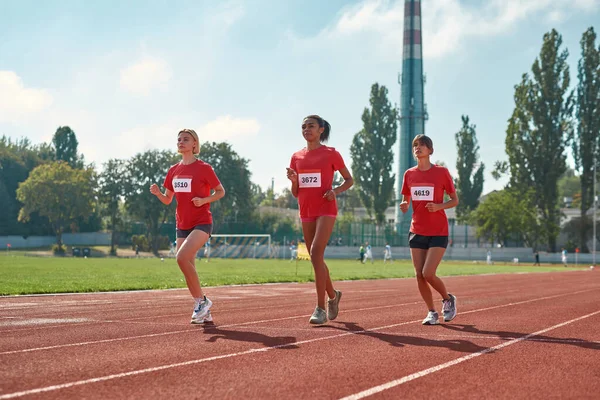 Full längd skott av atletiska unga kvinnor som springer tillsammans under mästerskapet på banan och fältet på arenan på en sommardag — Stockfoto