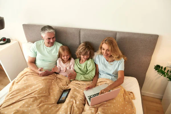 子供と幸せな両親はベッドの中でオンライン映画を見る — ストック写真