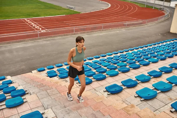 Motive olmuş genç bayan koşucu kendini formda tutuyor, stadyumda antrenman yapıyor.