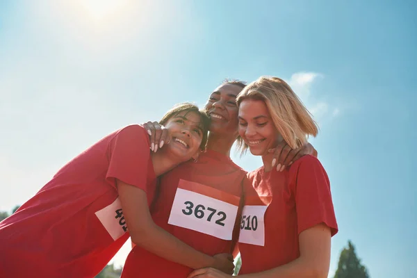 Porträtt av glada unga professionella kvinnliga löpare bär t-shirts med nummer står tillsammans, redo för maraton — Stockfoto
