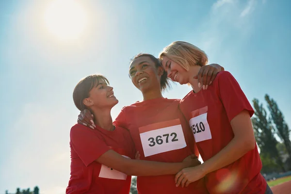 Porträtt av glada olika unga kvinnliga idrottare bär t-shirts med nummer står tillsammans, redo för maraton — Stockfoto