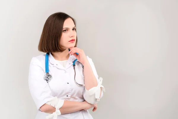 Portrait of beautiful young doctor with pensive face on light background Royalty Free Stock Images